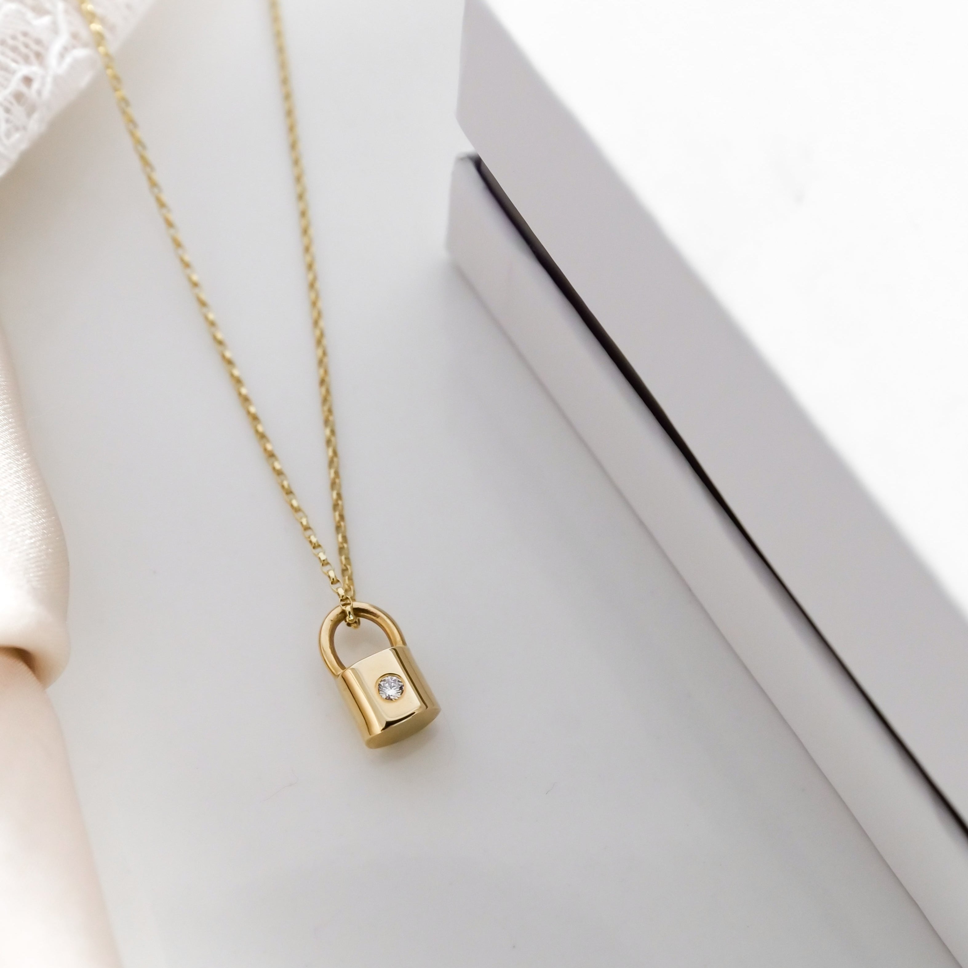 Gold necklace with a lock-shaped pendant on a white surface