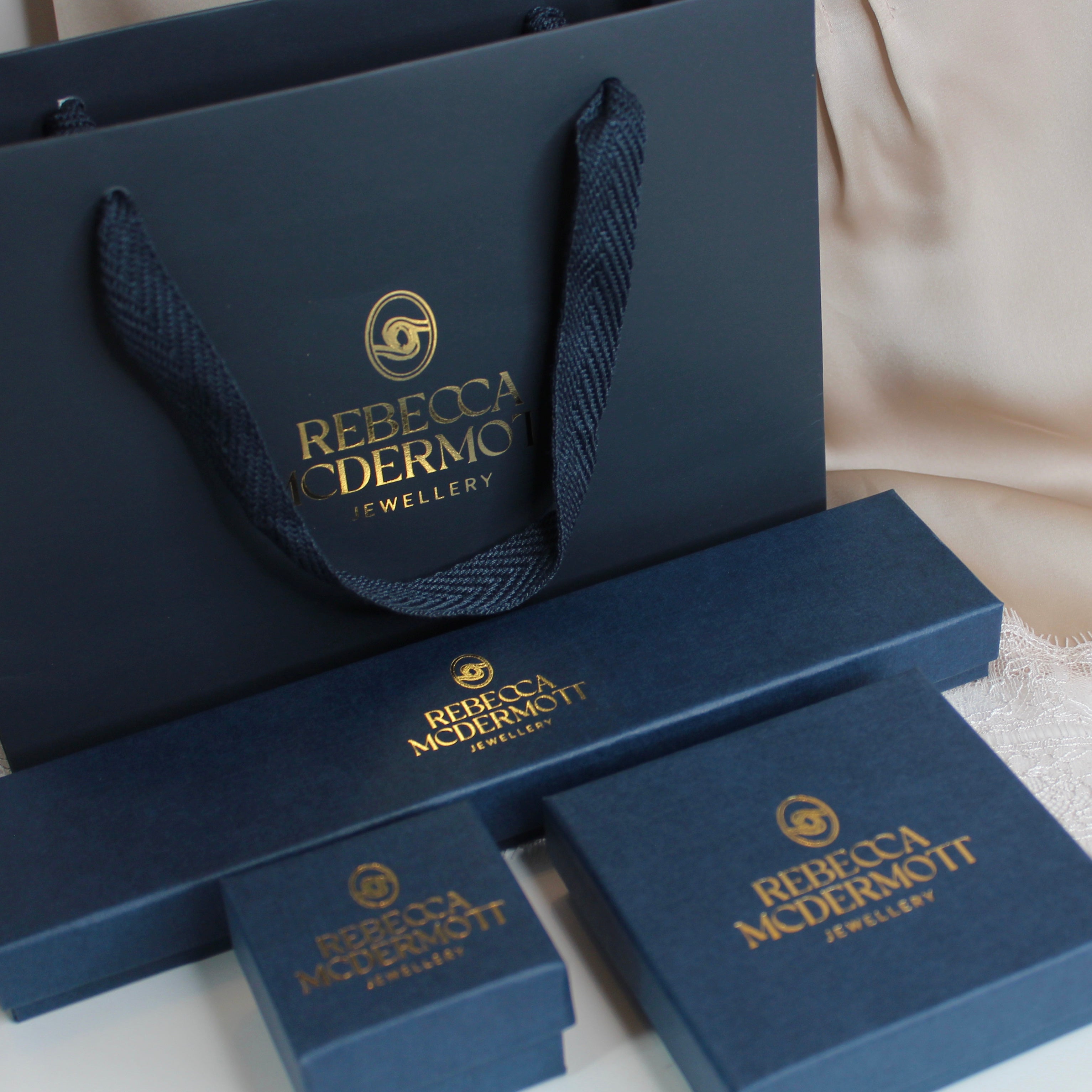 Rebecca McDermott Jewellery packaging including a navy blue bag and boxes on a light background.