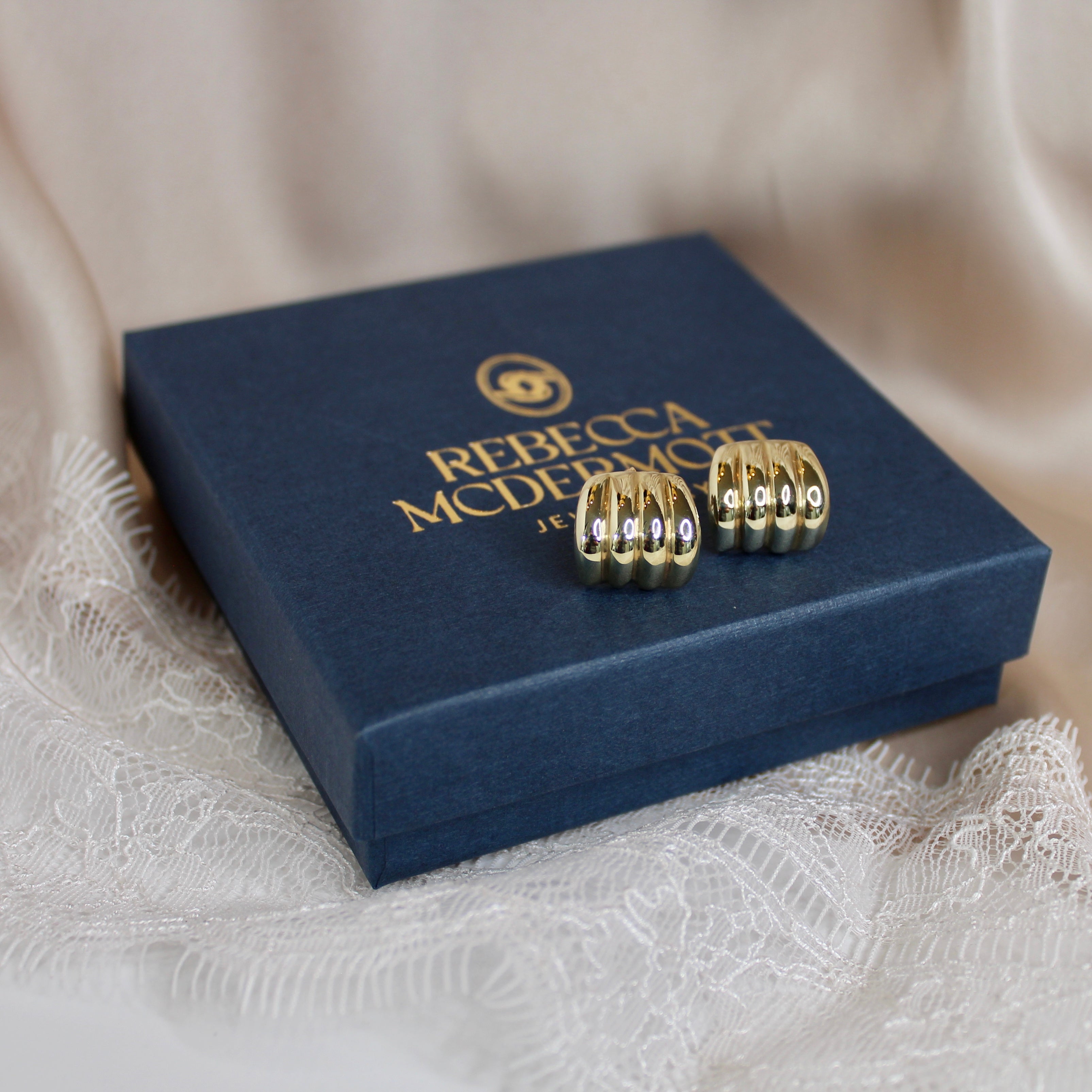 Gold earrings on a Rebecca Minkoff jewelry box with a soft beige background
