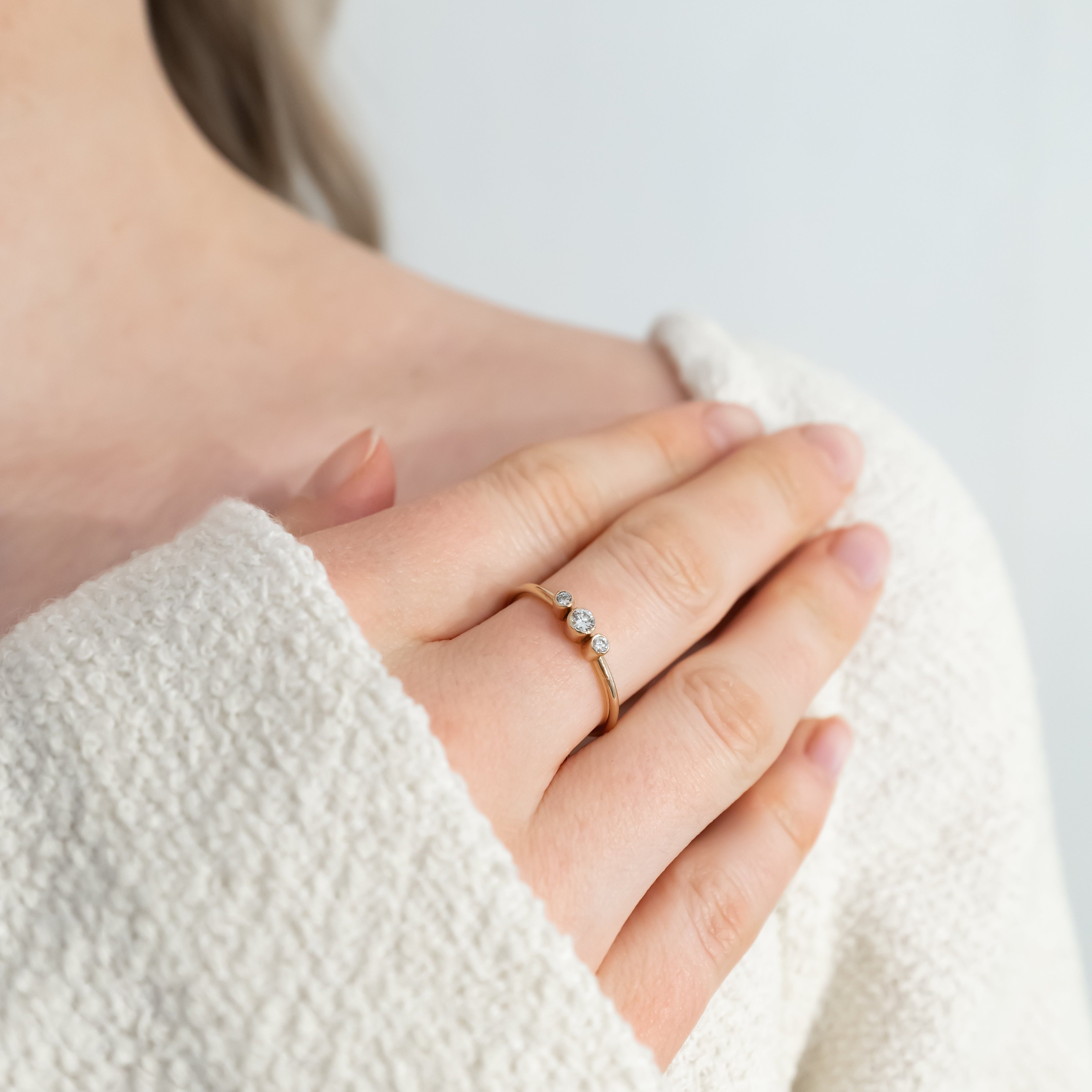 Close-up of a hand wearing a gold ring with a diamond on a light background