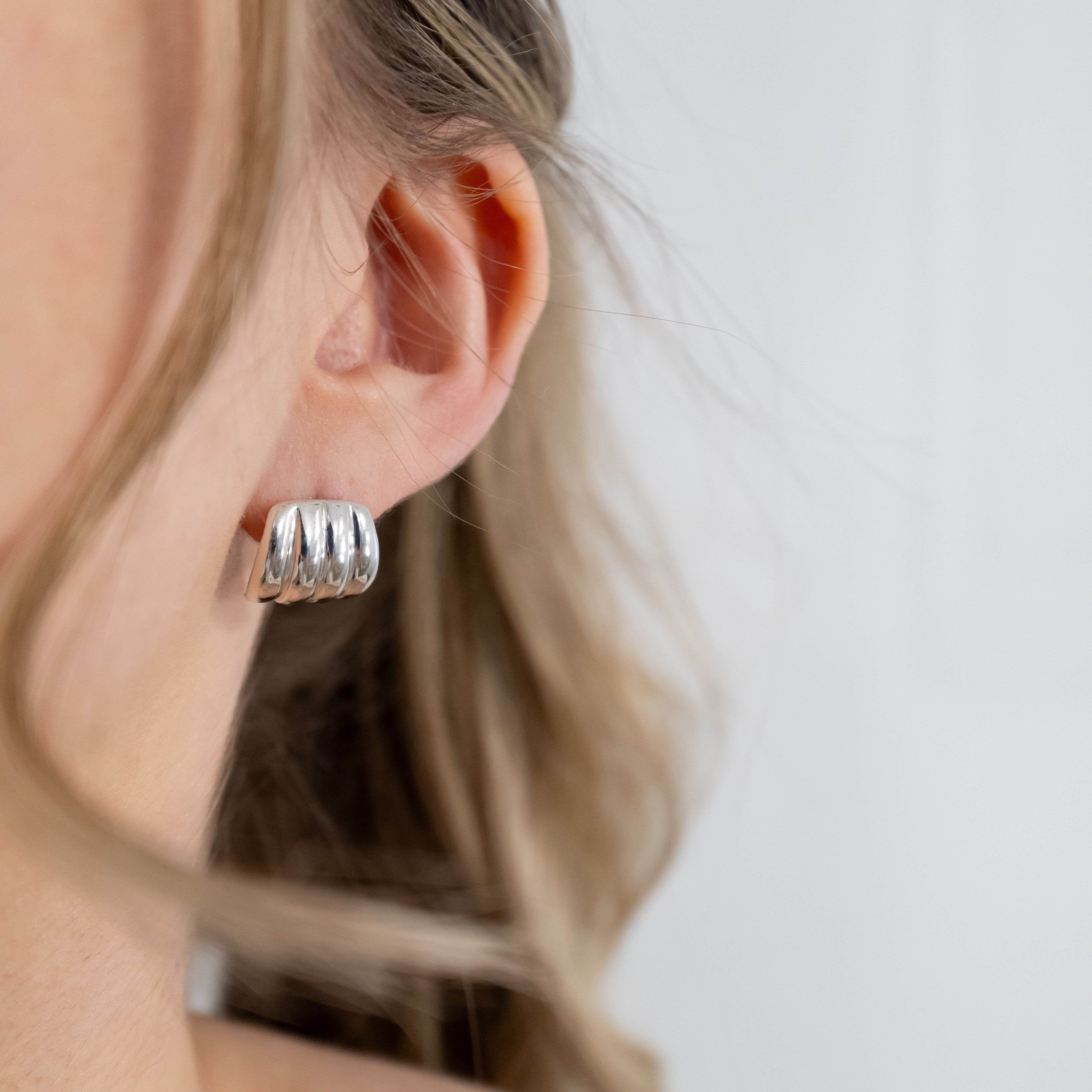 Close-up of a person wearing silver hoop earrings with a neutral background